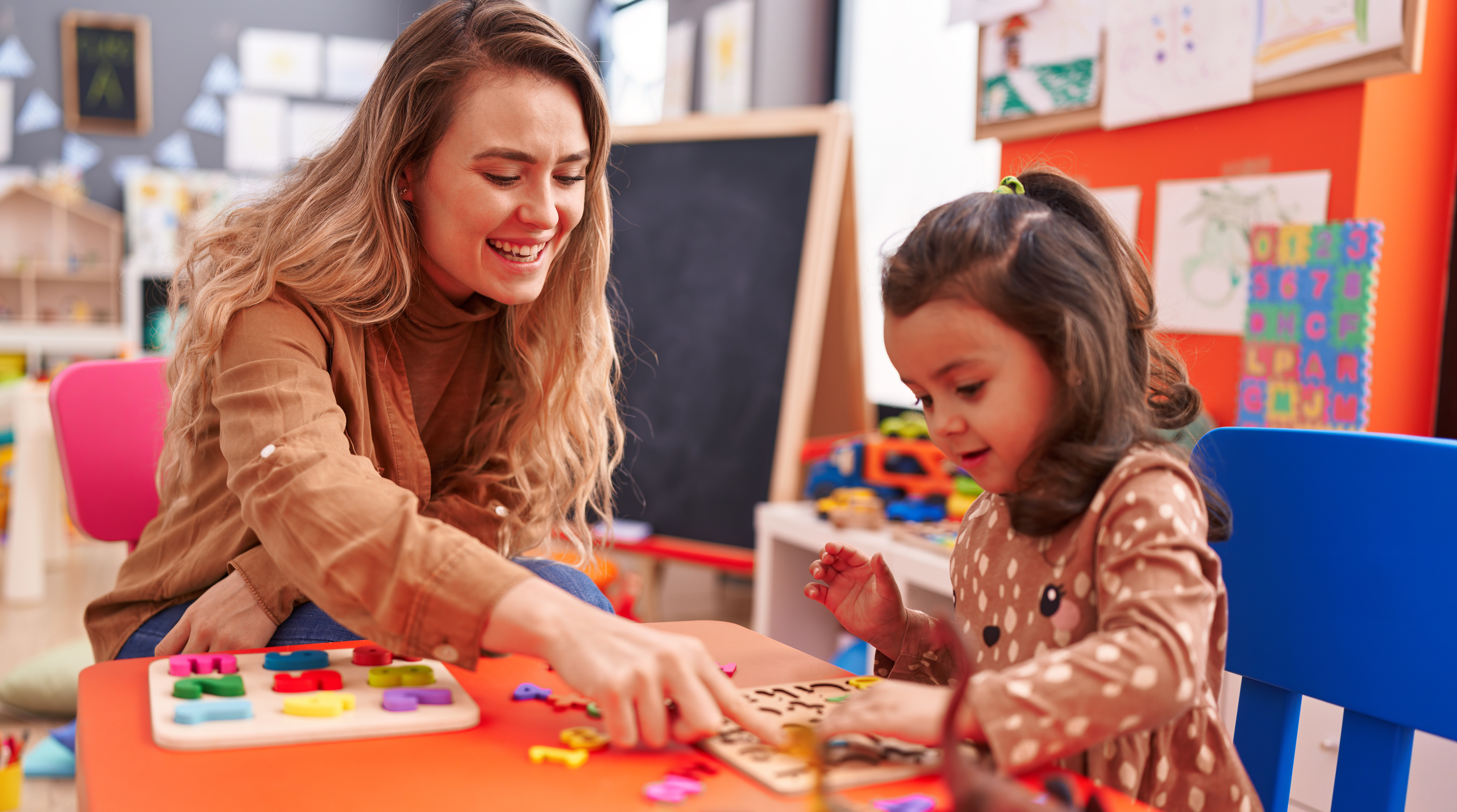 Teacher and toddler playing with maths puzzle game sitting on table at kindergarten Teacher and toddler playing with maths puzzle game